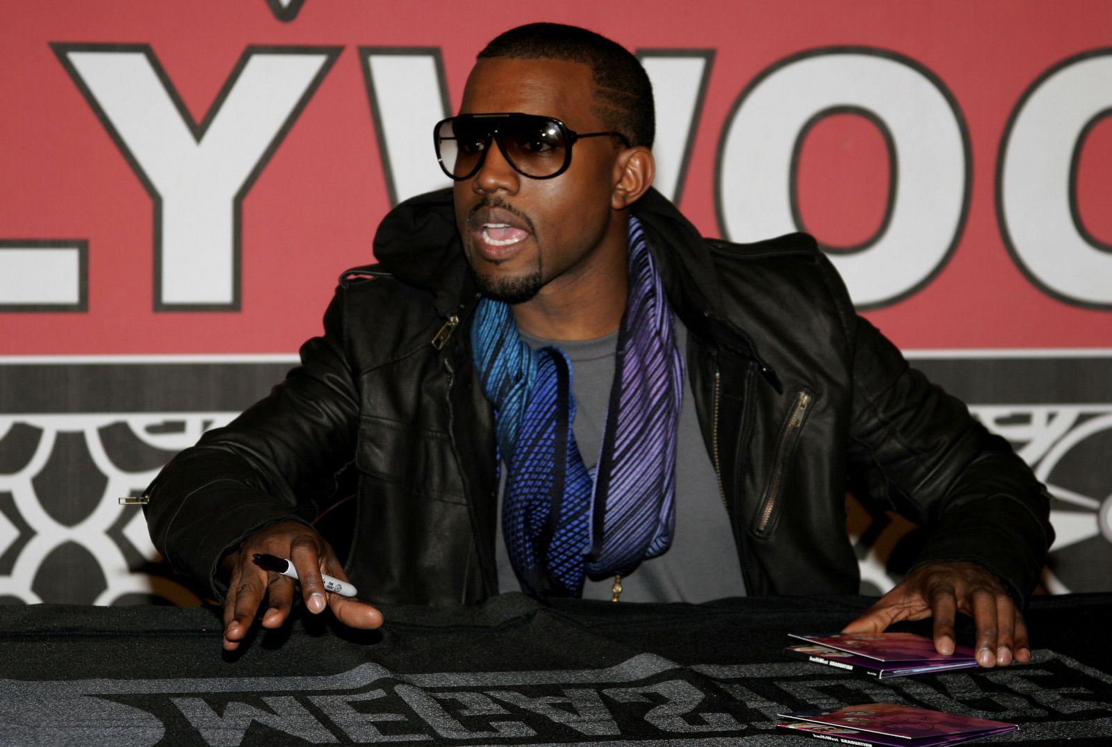 Kanye West olhando para o lado e segurando uma caneta para autografar 
