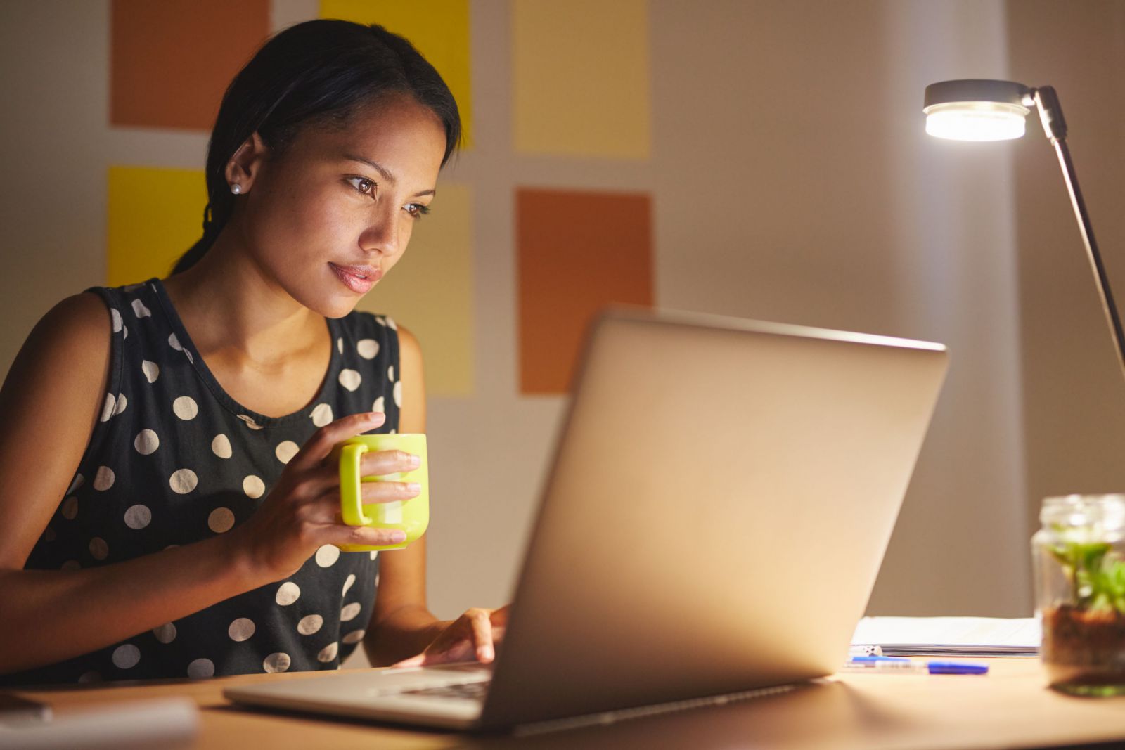 Mulher trabalhando em frente a um computador, enquanto segura uma xícara.