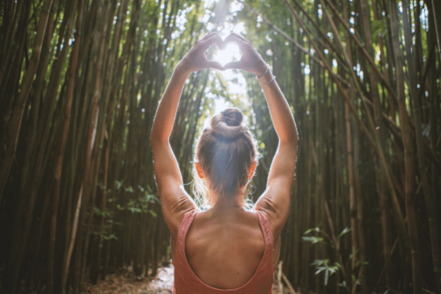 Mulher de costas em meio a natureza fazendo um coração com a mão