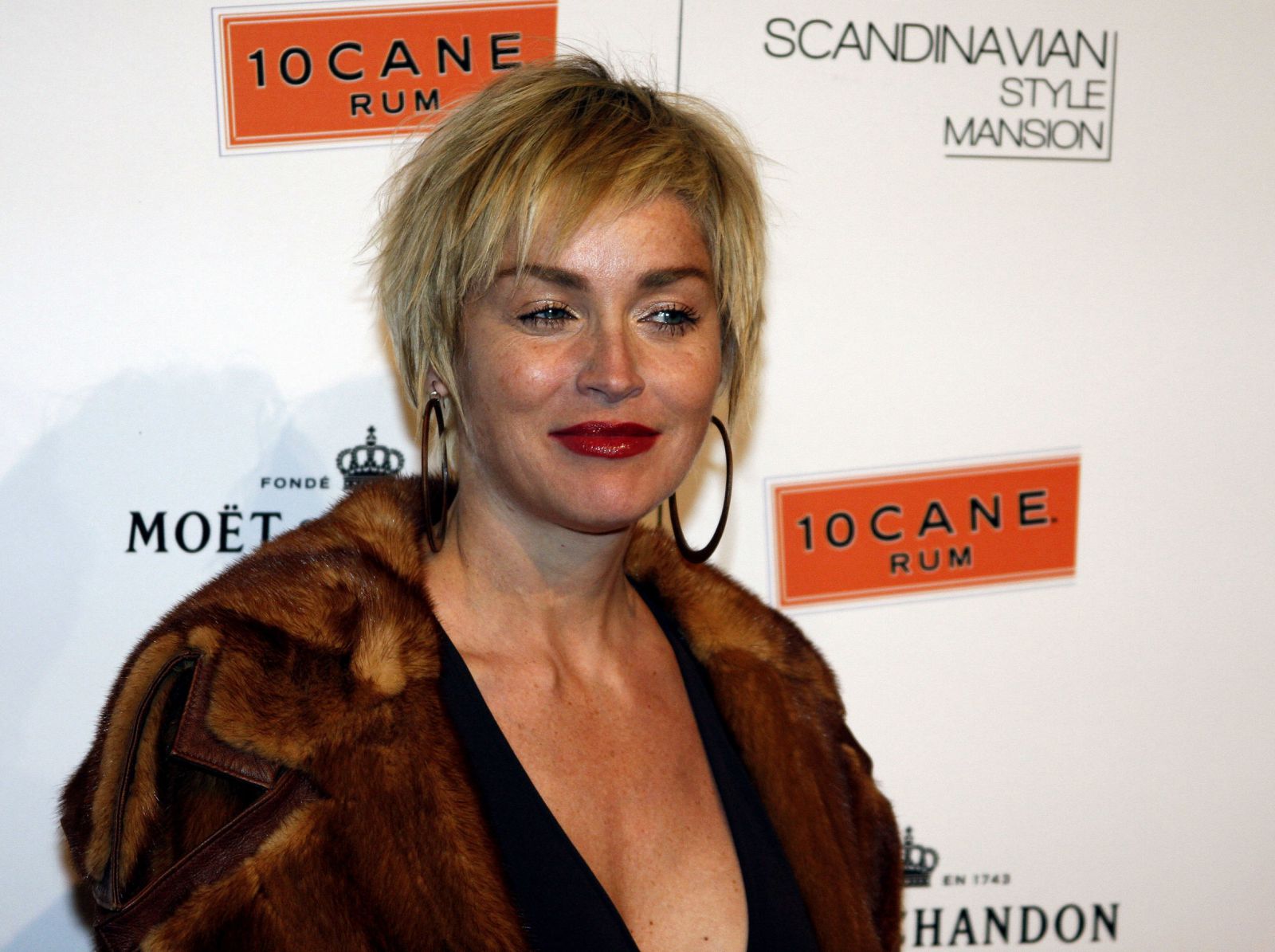 Sharon Stone olhando para o lado e sorrindo usando casaco de pele