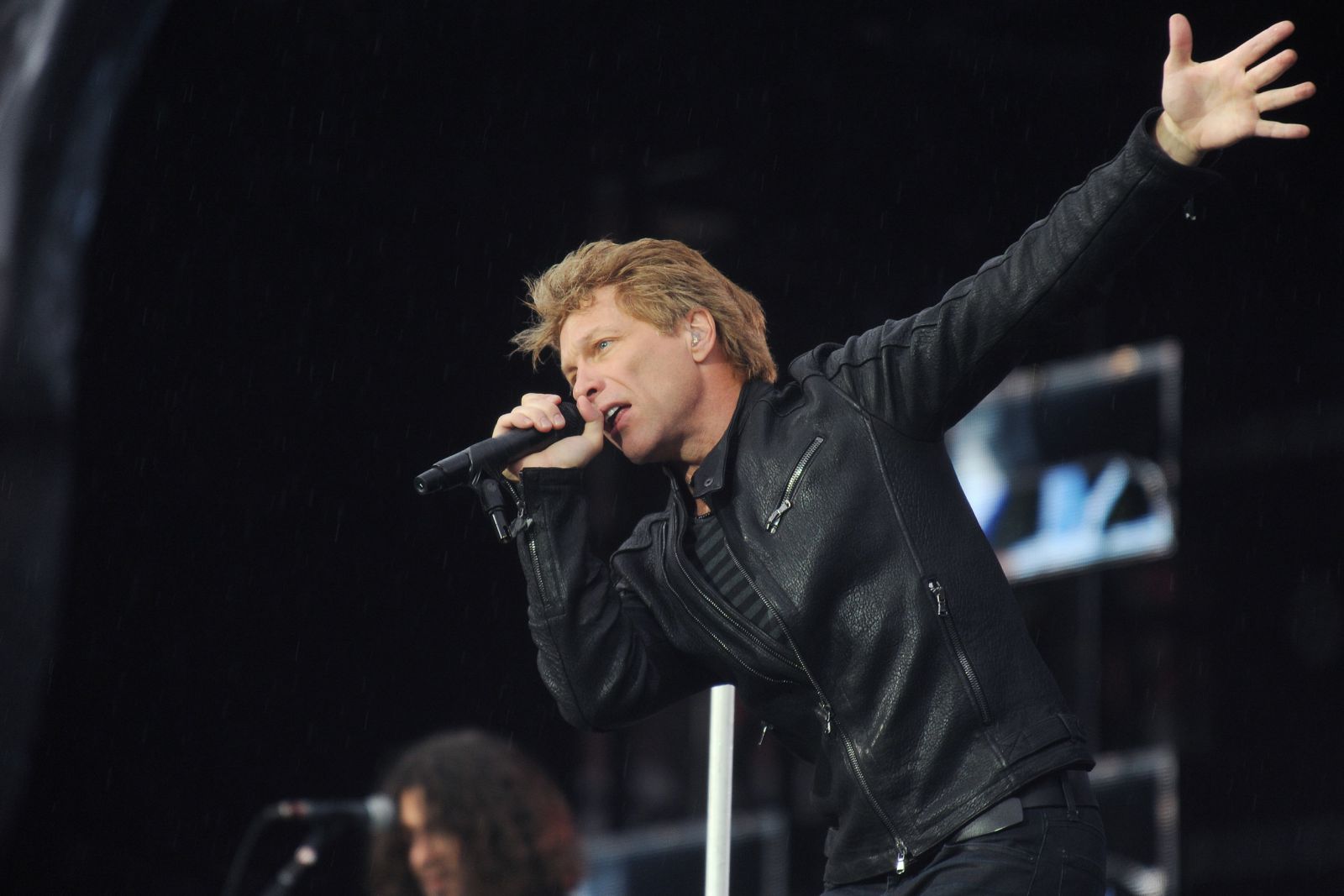 Jon Bon Jovi cantando no palco segurando microfone