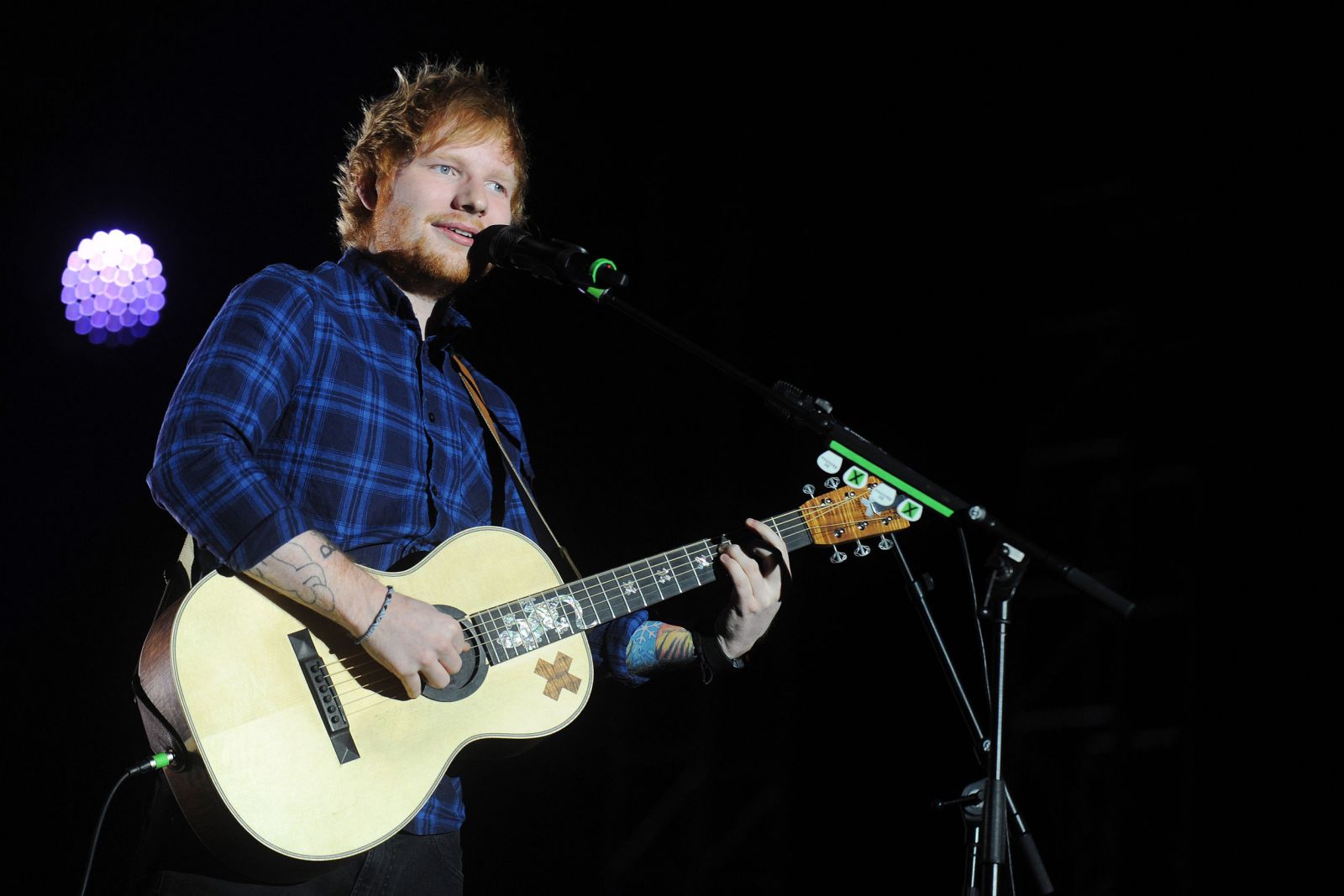 Ed Sheeran cantando e tocando violão em um palco