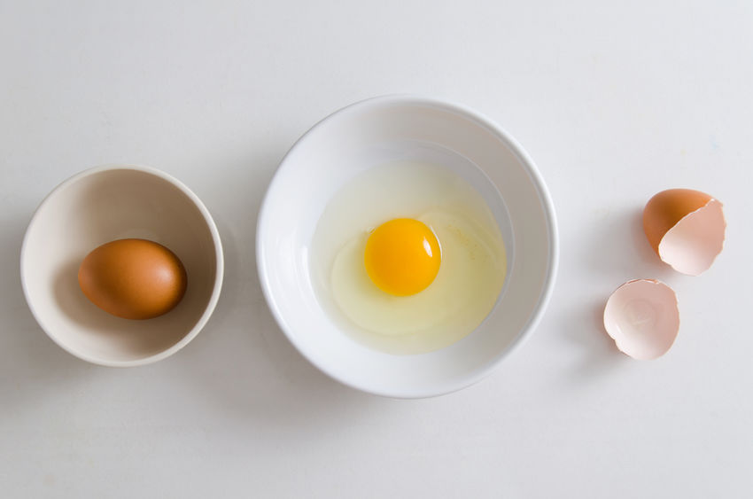 Tigela com um ovo inteiro, prato com gema e clara de ovo e cascas de ovo ao lado
