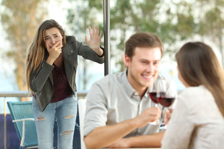 Homem e mulher brancos segurando taça de vinho, outra mulher branca ao fundo com expressão devastada.