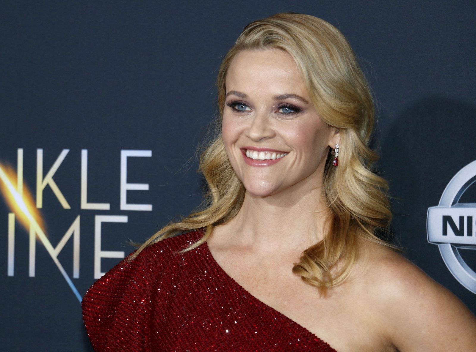 Reese Witherspoon olhando para frente e sorrindo com cabelo curto atrás das orelhas