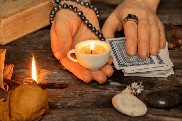 Mãos brancas segurando uma vela e sobrepostas em um baralho de tarot. Conceito de ocultismo e espiritualidade.