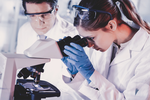 Jovens pesquisadores olhando sobre microscópio alguma de suas pesquisas, em laboratório de ciência. 