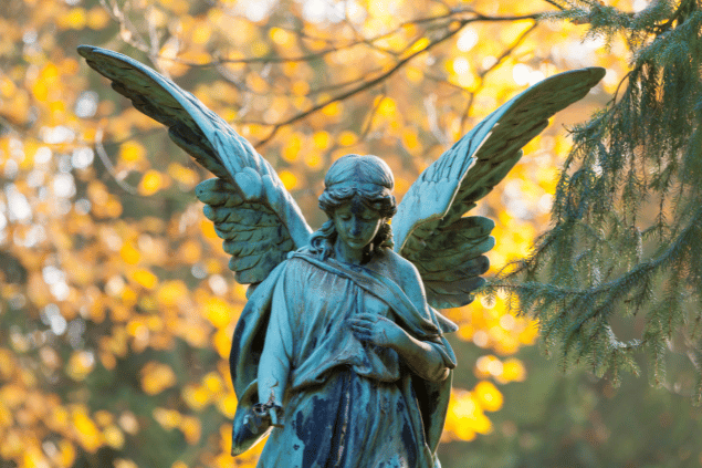 horstgerlach / Getty Images Signature / Canva Pro Imagem representativa do anjo da guarda Nanael. A estátua de anjo está em uma floresta com folhas amarelas.