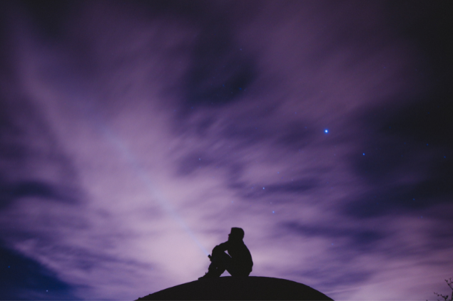 Silhueta de um homem sentado observando um céu todo estrelado