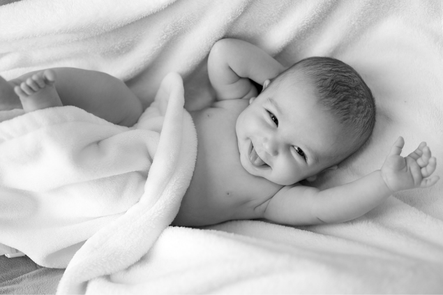 Foto em preto e branco de bebê deitado sorrindo e com a língua para fora