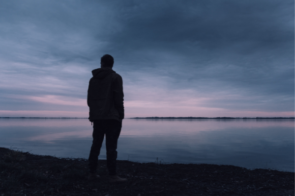 Homem em pé olhando o horizonte em frente a um lago