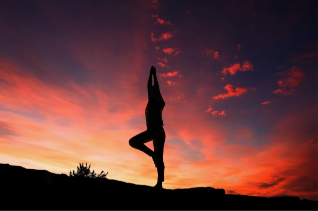 Silhueta de uma mulher em posição de yoga no pôr do sol