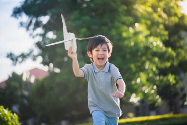 Menino brincando com um avião de papelão no meio de um parque