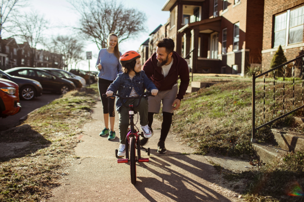 Homem ajudando um menino a andar de bicicleta em uma calçada cercada por grama