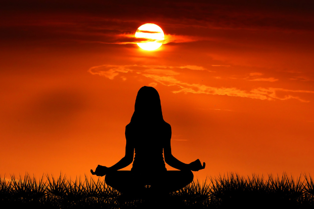 Mulher sentada meditando durante um pôr do sol 