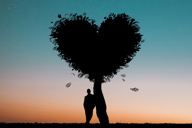 Homem apoiado em uma árvore que faz um símbolo de coração com suas folhas