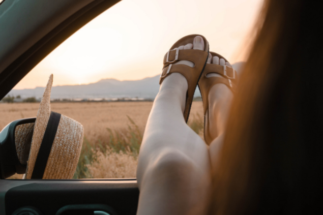 Mulher de sandália com os pés para fora da janela do carro