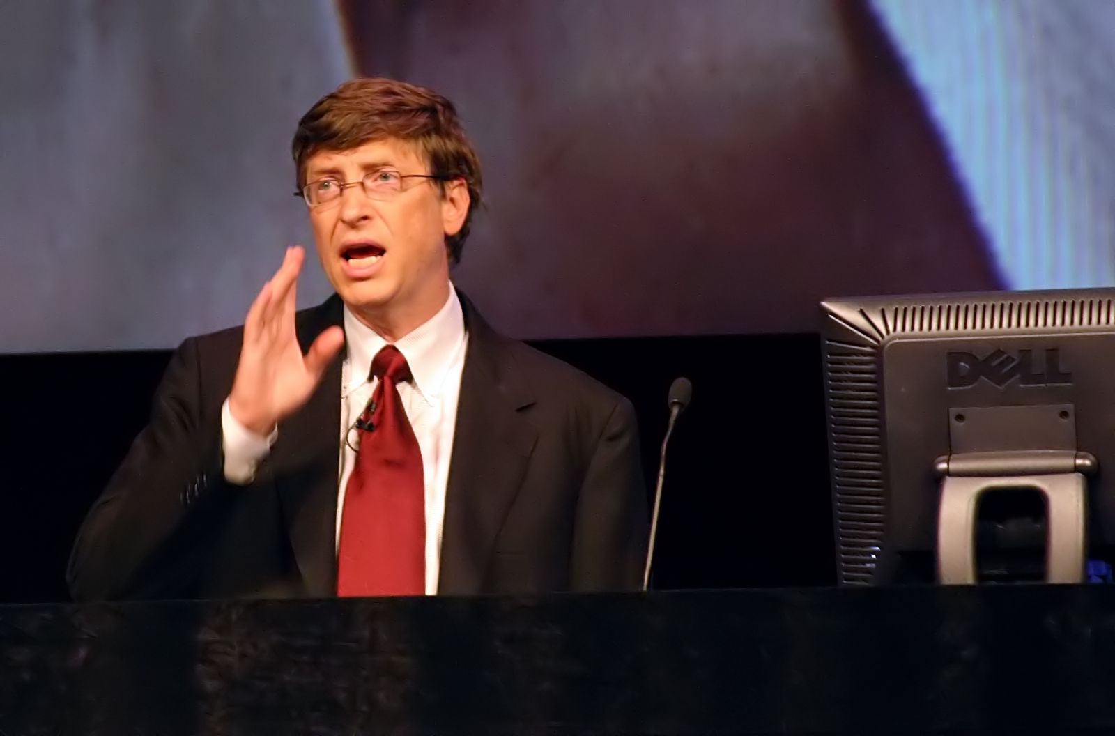 Bill Gates usando terno e gravata em um palco 