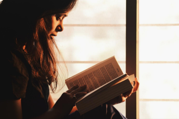 Mulher lendo livro ao lado de uma janela