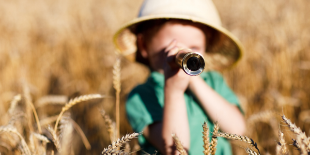 Menino no meio do campo com binóculo