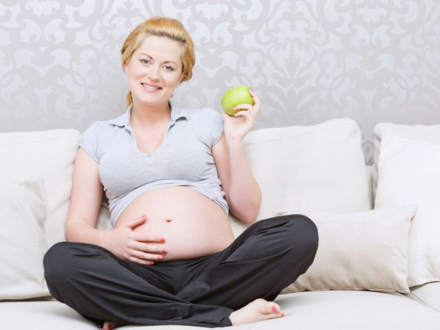 Mulher grávida sorrindo e segurando maçã