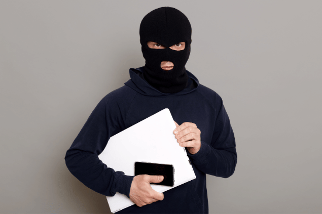 Ladrão segurando celular e notebook roubados. 