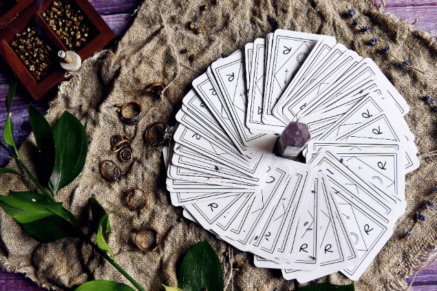 Algumas cartas de Tarot viradas para baixo estão em destaque na imagem. Ao lado, há um cristal e outros objetos.