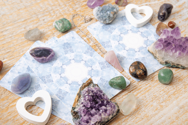 FotoHelin / FotoHelin Images / Canva Algumas cartas de Tarot viradas para baixo estão em destaque na imagem. Ao lado, há cristais e outros objetos.