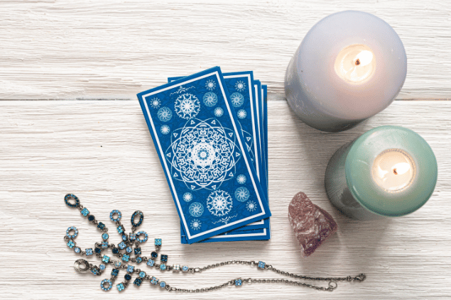 HappyNati / Getty Images / Canva Algumas cartas de Tarot viradas para baixo estão em destaque na imagem. Ao lado, há duas velas e outros objetos.