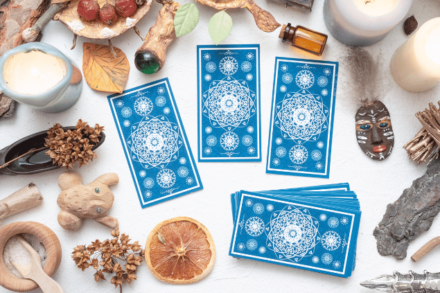 HappyNati / Getty Images / Canva Algumas cartas de Tarot viradas para baixo estão em destaque na imagem. Ao lado, há velas e outros objetos.