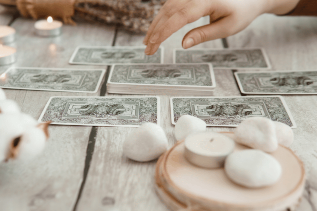 Изображения пользователя annu1tochka / Canva Algumas cartas de Tarot viradas para baixo estão em destaque na imagem. Ao lado, há velas e outros objetos.