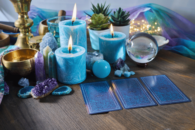 Vetrestudio / Canva Algumas cartas de Tarot viradas para baixo estão em destaque na imagem. Ao lado, há velas e outros objetos.