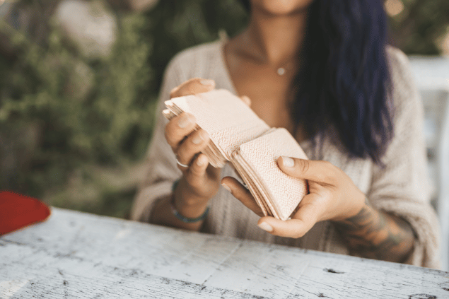 As mãos de uma taróloga segurando cartas de Tarot viradas para baixo estão em destaque na imagem.