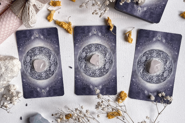 Veronika Malchevska / Pexels / Canva Algumas cartas de Tarot viradas para baixo estão em destaque na imagem. Ao lado, há flores e outros objetos.