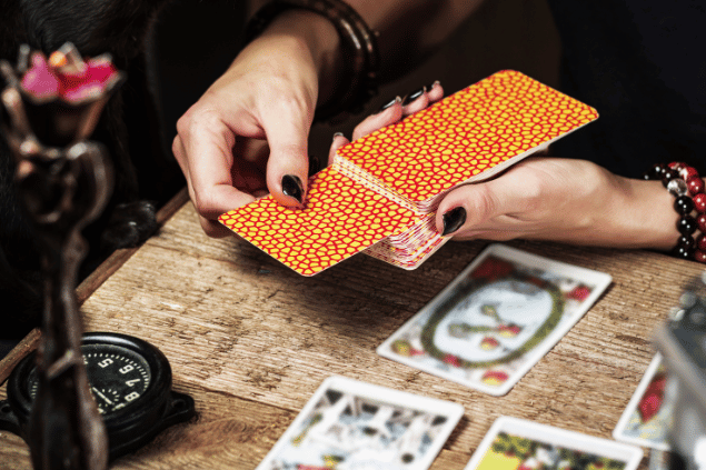 VladK213 / Getty Images / Canva As mãos de uma taróloga segurando cartas de Tarot viradas para baixo estão em destaque na imagem.