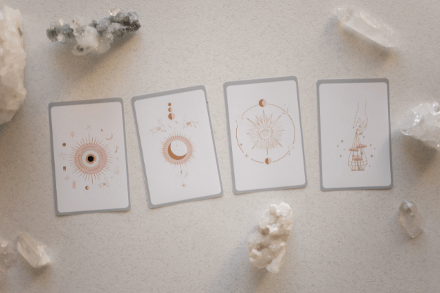 Katrin Bolovtsova / Pexels / Canva Algumas cartas de Tarot estão em destaque na imagem. Ao lado, há cristais.