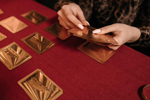 Pavel Danilyuk / Pexels / Canva As mãos de uma taróloga segurando cartas de Tarot viradas para baixo estão em destaque na imagem.