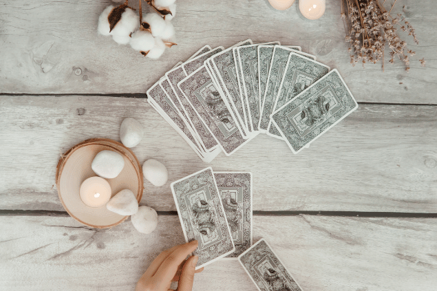 Algumas cartas de Tarot viradas para baixo estão em destaque na imagem. Ao lado, há velas e outros objetos.