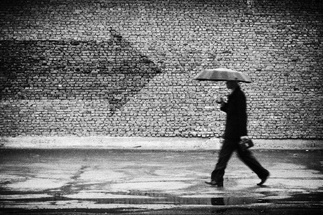 Imagem em preto e branco, ilustrando uma pessoa de guarda-chuva caminhando para uma direção e não parede tem a sobra de uma seta em direção contrária