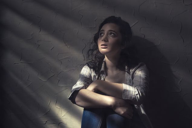 Mulher sentada no chão, na penumbra com feição de medo e choro