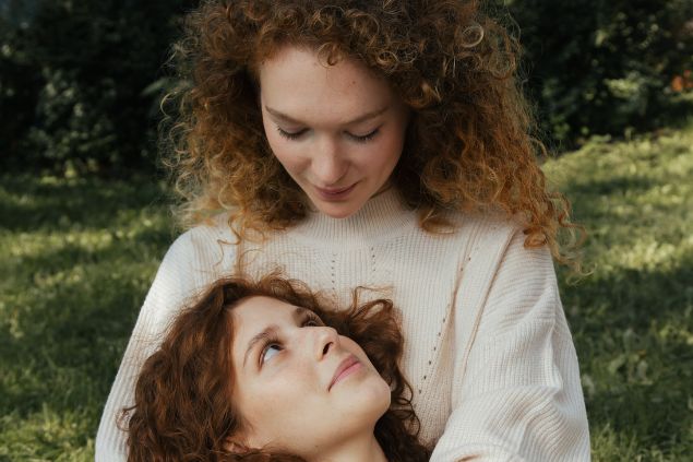 Imagem de um casal de mulheres, se olhando com olhar apaixonado, e uma está deitada no colo da outra