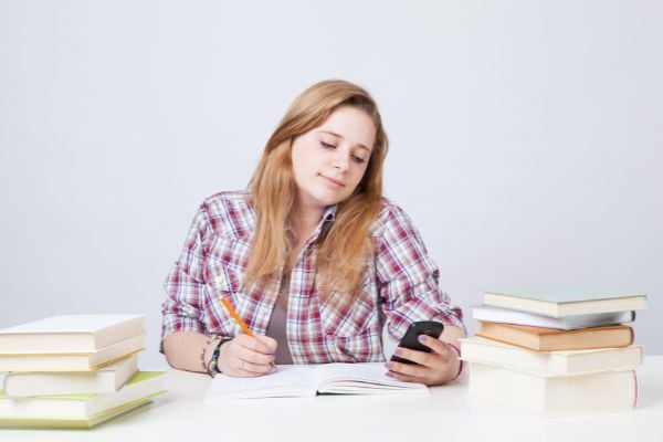 Menina distraída olhando celular enquanto estuda