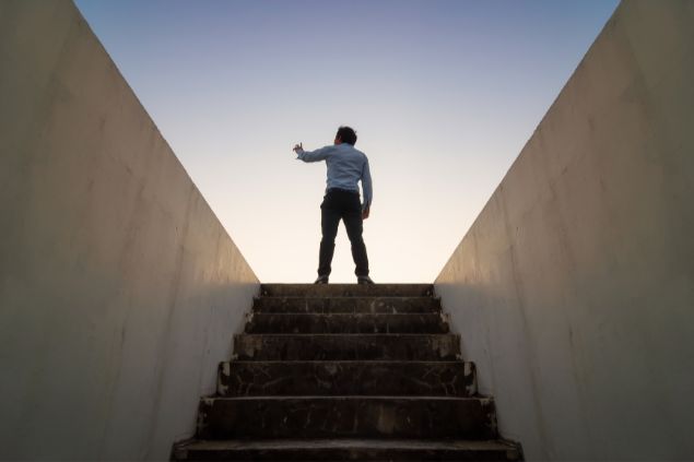 Imagem de um homem no topo da escada com o braço levantado em direção ao céu