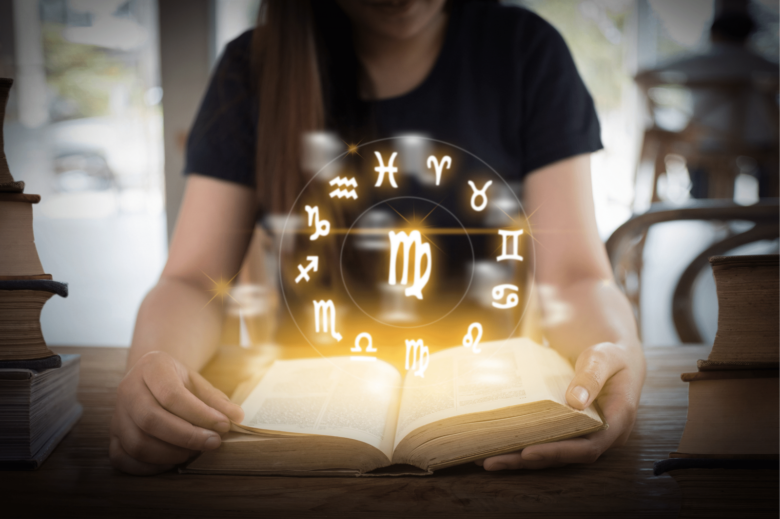 Mulher branca sentada lendo livro com símbolos do horóscopo brilhando.