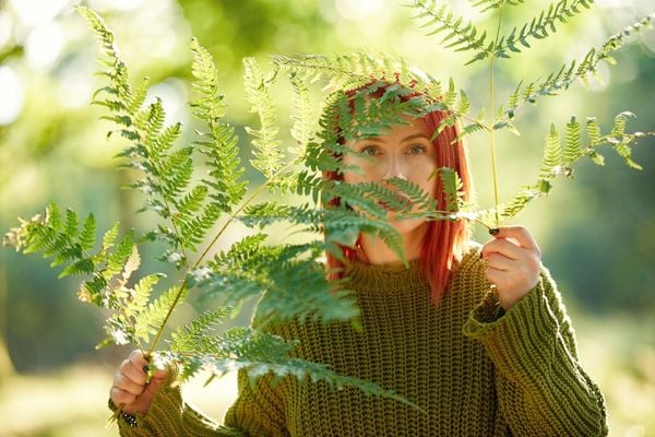 Mulher ruiva segurando folhas de samambaia na frente do rosto