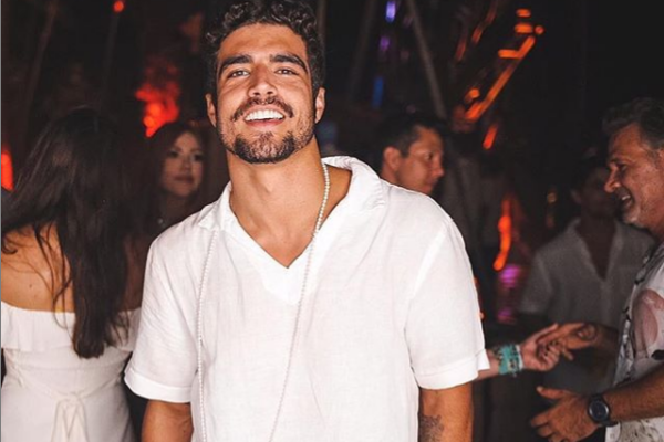 Caio Castro sorrindo em uma festa usando camiseta