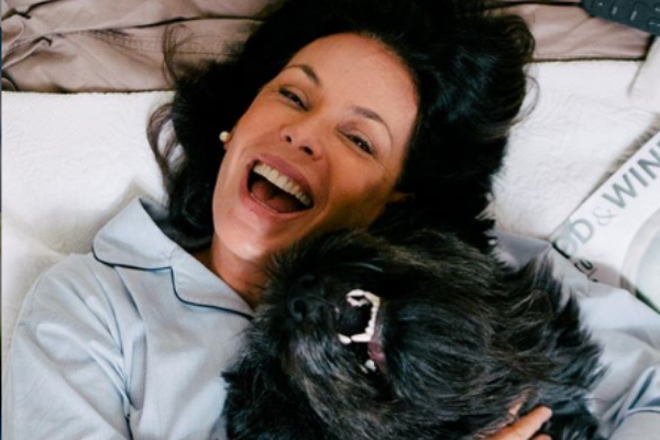 Carolina Ferraz deitada na cama sorrindo ao lado do cachorro