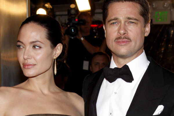 Angelina Jolie usando vestido ao lado de outro ator que está usando terno