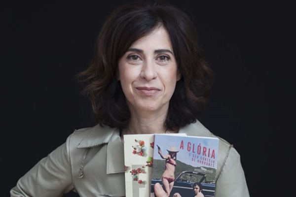 Fernanda Torres segurando alguns livros e sorrindo olhando para frente