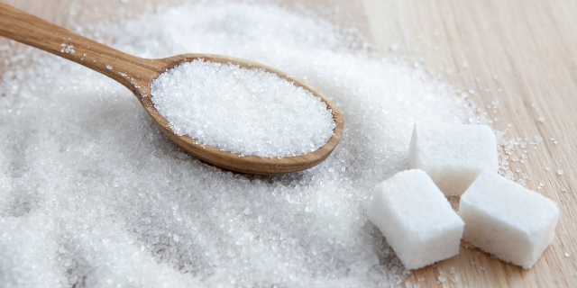 Açúcar espalhado em uma mesa, colher de madeira com açúcar e cubos de açúcar
